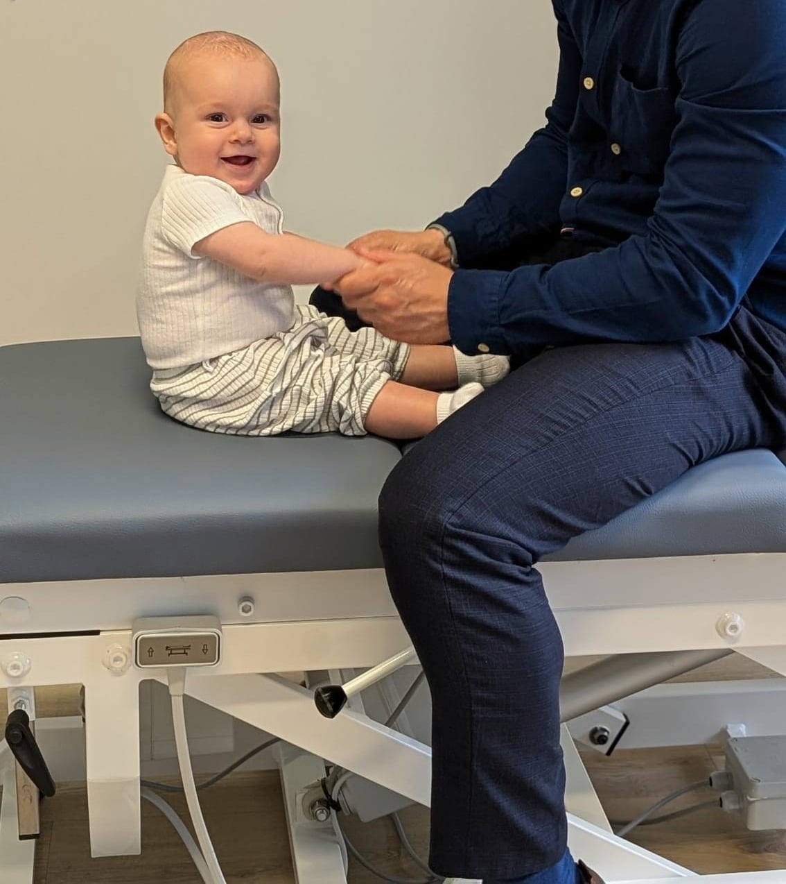 Dr Dane Jacks with a smiling baby sitting on the treatment table at Ocean City Chiropractic